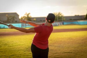 A young boy in a red shirt swings a baseball bat on a sunny field.