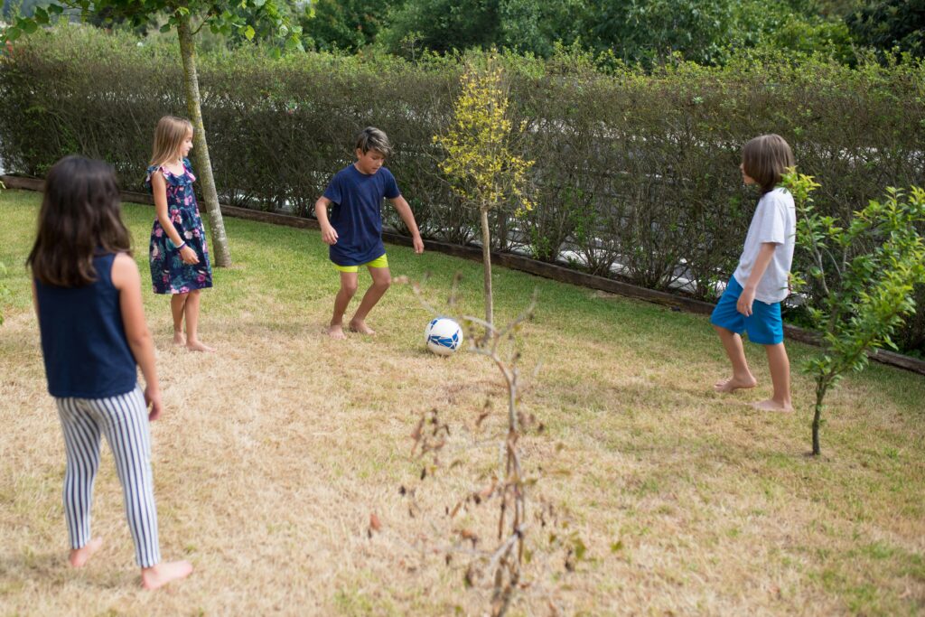 Group of kids enjoying a sunny day playing soccer in a grassy backyard.