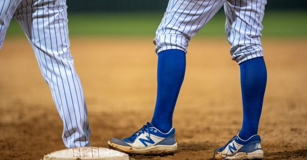 Close-up of baseball players wearing blue knee socks and sneakers at second base.
